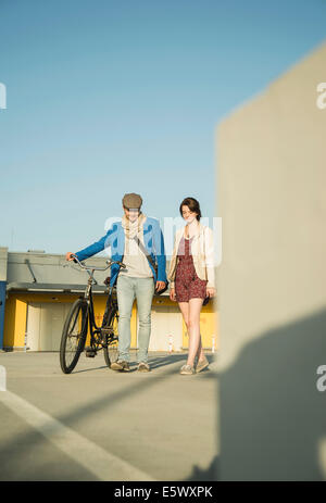 Coppia giovane spingendo in bicicletta lungo la strada Foto Stock