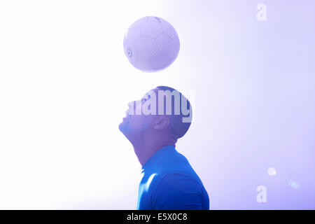 Studio shot del maschio giovane giocatore di calcio mantenendo la sfera metà aria con la testata Foto Stock