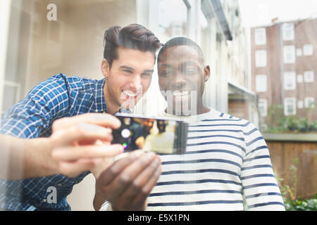 Due giovani amici maschi tenendo selfie patio dietro il vetro Foto Stock