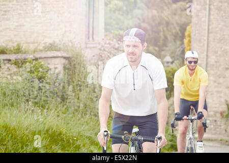 I ciclisti in sella attraverso il villaggio, Cotswolds, REGNO UNITO Foto Stock