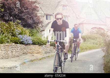 I ciclisti in sella attraverso il villaggio, Cotswolds, REGNO UNITO Foto Stock