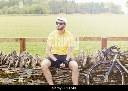 Ciclista seduto sul muro di pietra, Cotswolds, REGNO UNITO Foto Stock