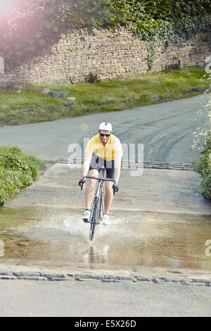 Ciclista a cavallo su strada allagata, Cotswolds, REGNO UNITO Foto Stock