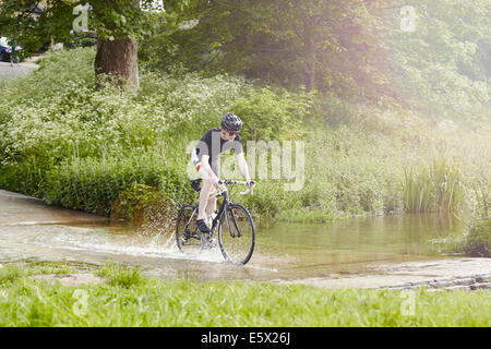 Ciclista a cavallo su strada allagata, Cotswolds, REGNO UNITO Foto Stock