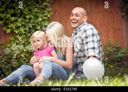 Felice coppia seduta con toddler figlia in giardino Foto Stock