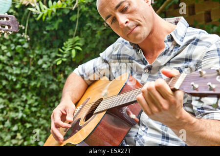 Metà uomo adulto suonare la chitarra acustica in giardino Foto Stock