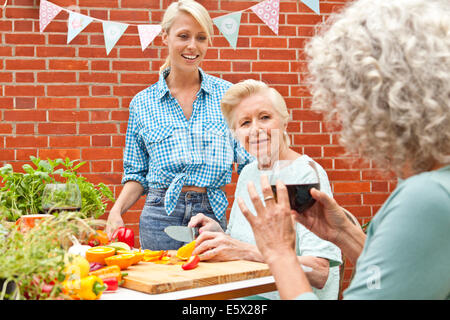 Tre generazioni di donne in chat durante la preparazione di cibo al tavolo da giardino Foto Stock