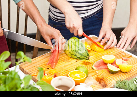 Le mani di tre donne la preparazione di frutta fresca al tavolo da giardino Foto Stock