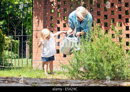 Toddler femminile aiutando la madre con annaffiatoio in giardino Foto Stock