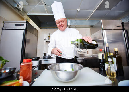 Immagine di chef maschio versando olio d'oliva nella ciotola in cucina Foto Stock