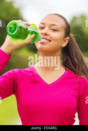 Donna sorridente di bere dalla bottiglia Foto Stock