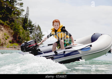 Ragazzo dello sterzo motore accelerando dinghy in mare Foto Stock