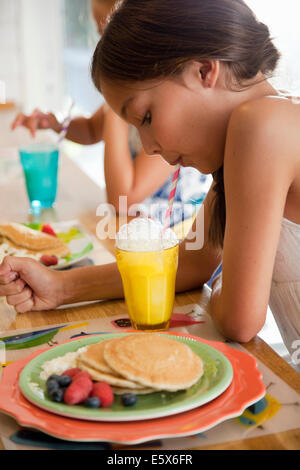 Due sorelle soffiare bolle attraverso cannucce al bar per la prima colazione Foto Stock