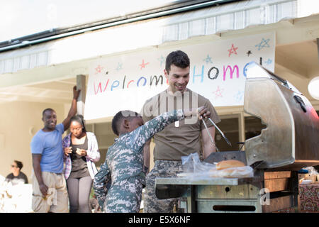 Ragazzo alla brace hamburger con soldato maschio a homecoming party Foto Stock