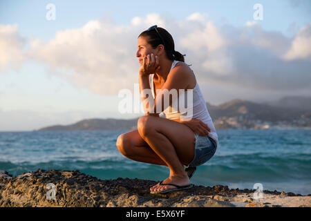 Metà donna adulta accovacciato e ammirate il mare dei Caraibi dal molo, Spice Island beach resort, Grenada, Foto Stock