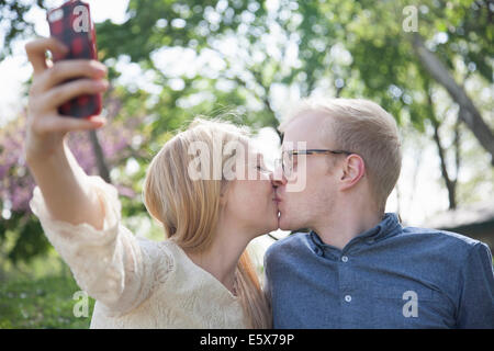 Coppia giovane in stazionamento tenendo selfie mentre baciare Foto Stock