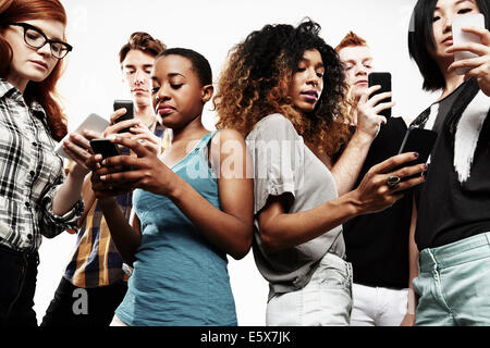 Basso angolo studio shot di sei giovani adulti texting sullo smartphone Foto Stock