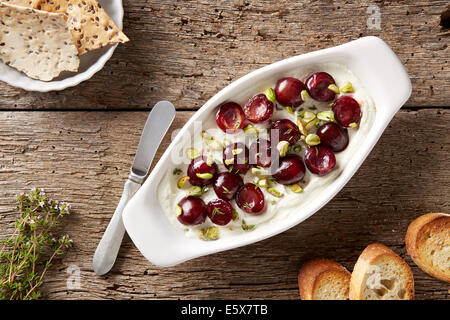 Formaggio di capra con ciliegie saltato, pistacchi e di timo fresco. Servita con pane e i semi di lino cracker Foto Stock