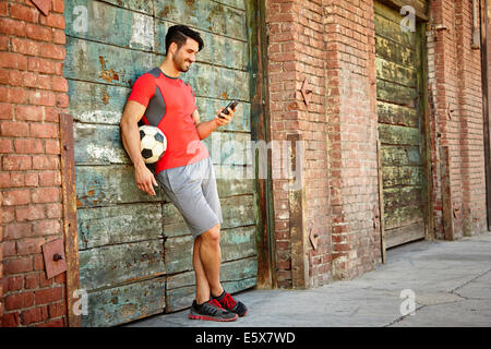 Maschio giovane giocatore di calcio texting sullo smartphone Foto Stock