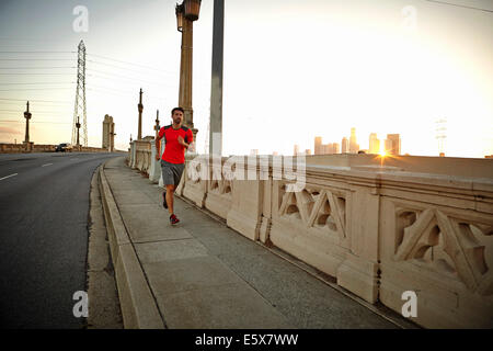 Giovane uomo che corre attraverso il ponte della città di sunrise Foto Stock