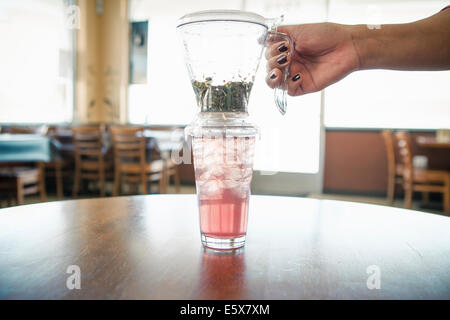 Mano femmina con iced tè alle erbe e il filtro in cafe Foto Stock