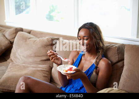 Giovane donna prendendo una pausa di formazione, mangiando frutta sul divano Foto Stock