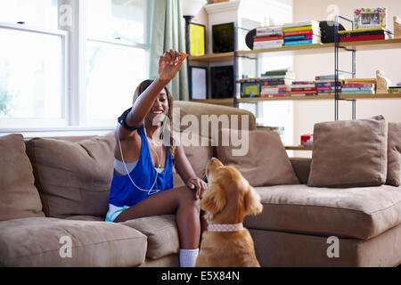 Giovane donna prendendo una pausa di formazione, tenendo in mano il biscotto per il cane in salotto Foto Stock