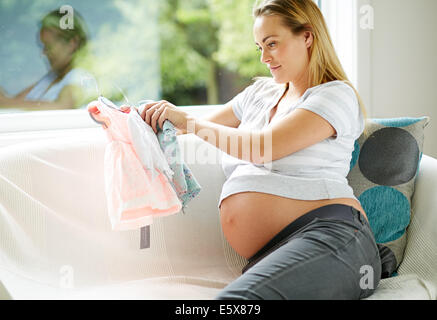 Donna incinta guardando vestiti del bambino Foto Stock