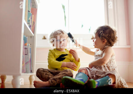 Toddler femmina maschio di spazzolatura toddlers capelli in sala giochi Foto Stock