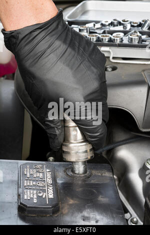 Un meccanico pulisce un terminale di batteria con un filo spazzola per terminali batteria durante la routine di manutenzione di automobili. Foto Stock