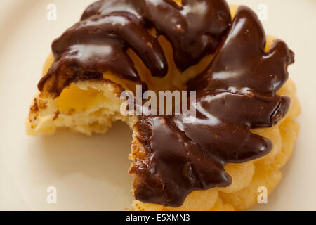 Un morso preso dal cioccolato francese smerigliato cruller ciambella Foto Stock