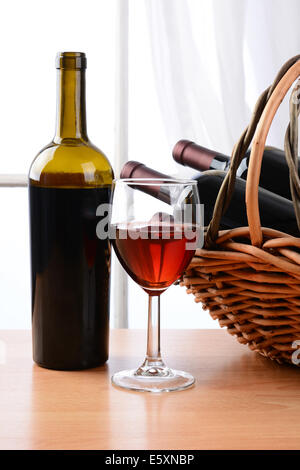 Vino ancora in vita con un paniere di bottiglie e un bicchiere di vino rosso davanti a una finestra con le tende. Formato verticale. Foto Stock