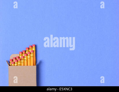Alta angolazione di una scatola di nuovo matite di colore giallo su una costruzione blu sullo sfondo della carta. Formato orizzontale con copia spazio. Foto Stock