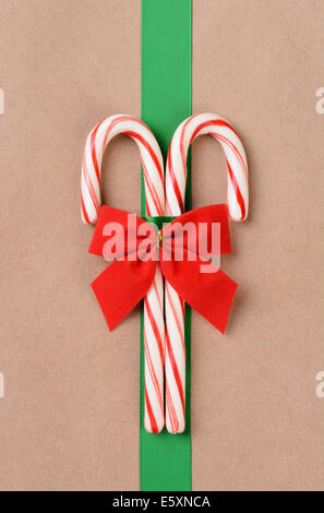 Due candy canes su una pianura carta marrone presente avvolto con un nastro verde e rosso di prua. Alta angolazione il riempimento del telaio in ver Foto Stock