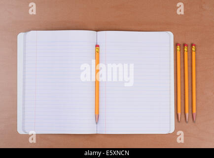 Un tema aperto libro con una matita in piega e tre più affilato matite a lato. Formato orizzontale su una classe di legno Foto Stock