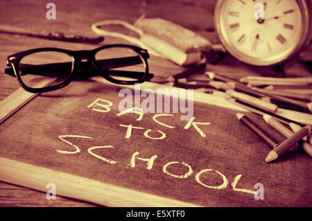 Una lavagna con la frase si torna a scuola scritto in esso, su un rustico scrivania in legno con un paio di occhiali e di altre scuole Foto Stock