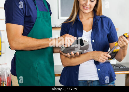 Lavoratore scorrendo carta di credito con la donna tenendo premuto SET CACCIAVITE Foto Stock