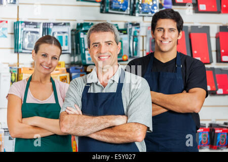 Gli addetti alle vendite in piedi con le braccia incrociate in hardware shop Foto Stock