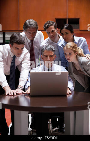 Business Associates si affollano attorno a un collega guardando sopra la sua spalla al computer portatile Foto Stock