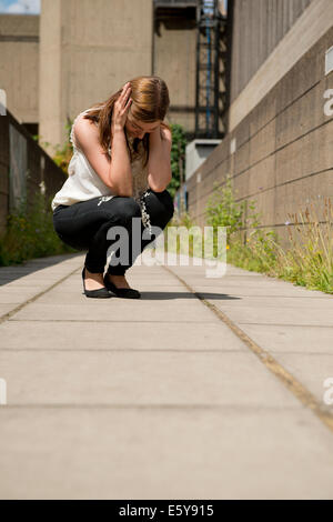 Sottolineato/teary giovane donna,accovacciato con la sua testa con le mani. Foto Stock