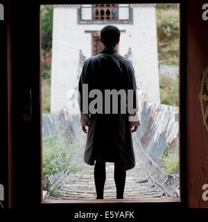 Il Bhutan man standing in forfront del Tamchhog Lhakhang ferro ponte di sospensione, Bhutan Foto Stock