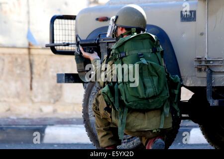 Un soldato israeliano si accovaccia vicino a una jeep militari armati con un M-16 pistola, rivolta a giovani palestinesi. Venerdì pomeriggio è stata dichiarata una rabbia in tutta la Cisgiordania. Nelle prime ore del mattino, dopo 8 A.m., la 72 Ore di cessate il fuoco tra Gaza e Israele si è conclusa e lottare contro la ripresa. Nelle prime ore della sera le forze israeliane hanno sparato e ucciso Ahmad Mohammad al-Qatar da al Amari Refugee Camp vicino a Ramallah, come le proteste hanno continuato nella solidarietà per la Striscia di Gaza in Cisgiordania. Oltre 40 persone sono rimaste ferite a Hebron durante le proteste. Nel frattempo, le incursioni aeree israeliane ucciso un bambino nel primo pomeriggio nel ne Foto Stock