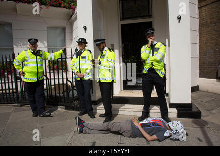 Londra, Regno Unito. Sabato 9 agosto 2014. Al di fuori di un ufficio pensato per essere utilizzato da Tony Blair, manifestanti sdraiarsi sul terreno come guardia di polizia locali. Pro-Palestinian manifestanti nella loro decine di migliaia di marzo attraverso il centro di Londra all'Ambasciata americana in segno di protesta contro l'offensiva militare a Gaza da parte di Israele. I cittadini britannici e British palestinesi raccolte in numero enorme portando cartelli e striscioni chiamando per 'Free Palestine' e di 'fine l assedio a Gaza". Credito: Michael Kemp/Alamy Live News Foto Stock