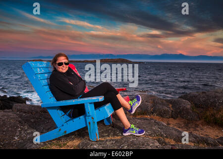 Ritratto di giovane donna seduta in blu Adirondack sedia-McNeil Bay, Victoria, British Columbia, Canada. Foto Stock