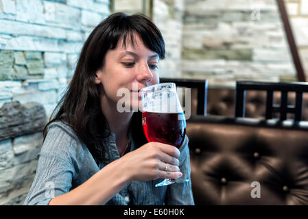 Ragazza seduta al bar con un bicchiere di birra di ciliegio Foto Stock