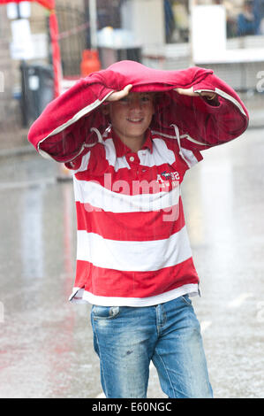 Brecon, Powys, Wales, Regno Unito. Il 10 agosto 2014. Un giovane ragazzo ripari sotto il suo hoodie come pioggia colpisce Brecon l'ultimo giorno del trentesimo Brecon Jazz Festival. Credito: Graham M. Lawrence/Alamy Live News. Foto Stock