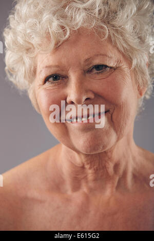 Colpo di Testa di attraenti senior donna faccia con un dolce sorriso contro uno sfondo grigio. Positivo donna matura. Foto Stock