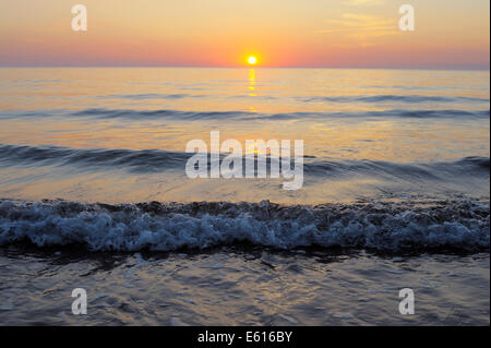Impostazione di Sun nel mare con piccole onde, Wales, Regno Unito Foto Stock