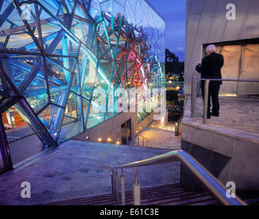 Uomo a Federation Square con il bordo illuminato il teatro al tramonto, Melbourne, Australia. Foto Stock