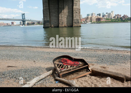 Un pianoforte abbandonati sulla formata naturalmente spiaggia sotto il ponte di Brooklyn sull'East River a Manhattan. Foto Stock